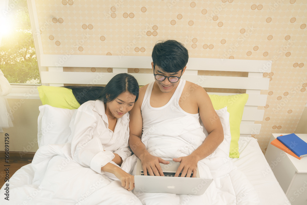 Obraz premium Young asian couple surfing the web from bed in the morning hours.
