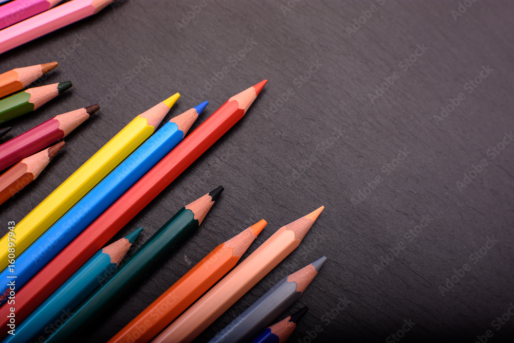 Many colored pencils on a black stone slate, place for text Many colored pencils on a black stone slate, place for text