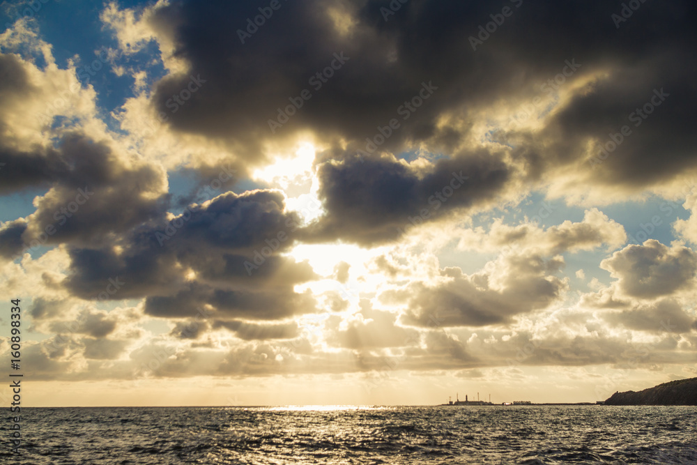 Beautiful sunset among the unimaginable clouds with glimpses of rays on the sea with waves