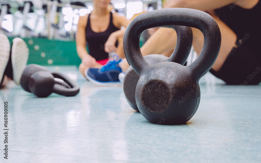 Φωτογραφία Closeup of black iron kettlebell and people group sitting on the floor of a fitn