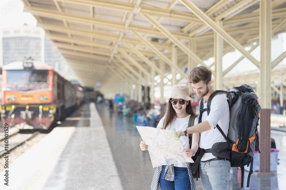 Young couple asian woman and caucasian man traveler are looking the map with train station background. Travel in summer concept. Young couple asian woman and caucasian man traveler are looking the map with train station background. Travel in summer concept.