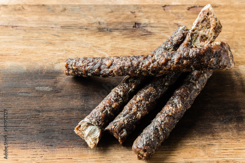 A Caucasian hand holding a stick of droewors (dried meat), this is a traditional food snack found in South Africa.
