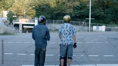 Two skateboarders high five each other and quickly set off down the road. Filmed from behind and dolly. photo