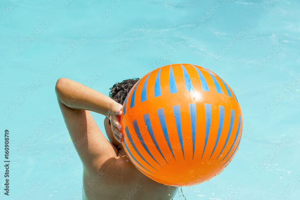 Boy ready to throw beach ball in swimming pool, seen from behind