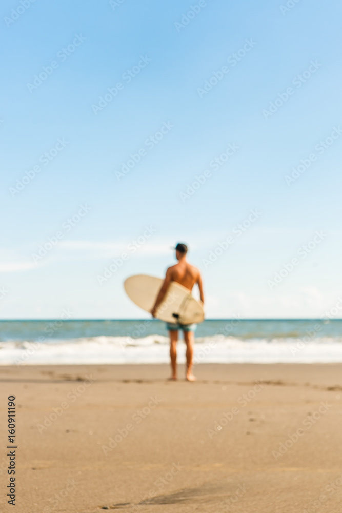 Out of focus, blurry image of handsome man stand with long surf surfing board wait for wave on surf spot at sea ocean beach. View from back. Concept of sport, freedom, new modern life, generation Y. Out of focus, blurry image of handsome man stand with long surf surfing board wait for wave on surf spot at sea ocean beach. View from back. Concept of sport, freedom, new modern life, generation Y.