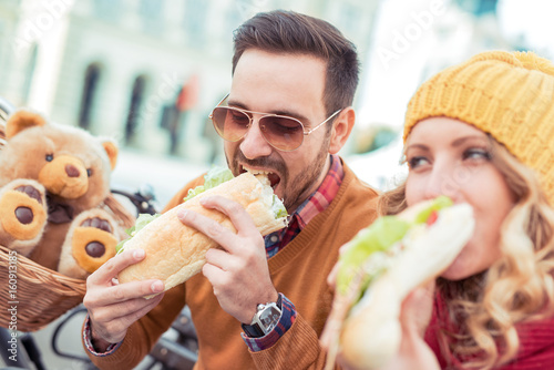 Cheerful romantic couple outdoors enjoying sandwiches