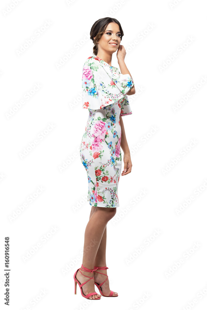 Gorgeous woman in floral dress with bun hairstyle touching hair smiling and looking away. Full body length portrait isolated on white background. Gorgeous woman in floral dress with bun hairstyle touching hair smiling and looking away. Full body length portrait isolated on white background.