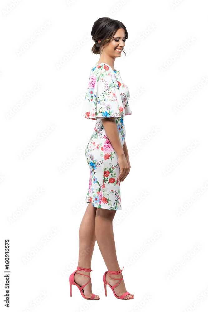 Elegant shy feminine fashion female model in floral dress smiling and looking down. Side view. Full body length portrait isolated on white background. Elegant shy feminine fashion female model in floral dress smiling and looking down. Side view. Full body length portrait isolated on white background.