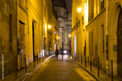 Two women walk in blurry motion at night on one of the streets of Le Marais district in Paris. It's night time. The district hosts many outstanding buildings of historic and architectural importance photo