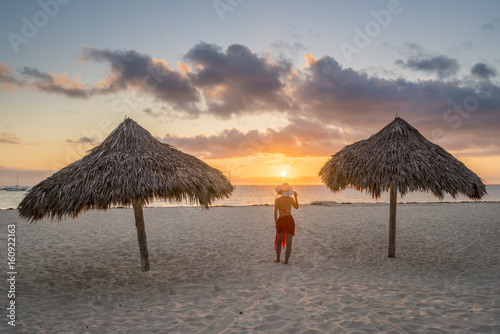 Bavaro Beach, Bavaro, Higuey, Punta Cana, Dominican Republic. Woman by thatch umbrellas on the beach at sunrise (MR).