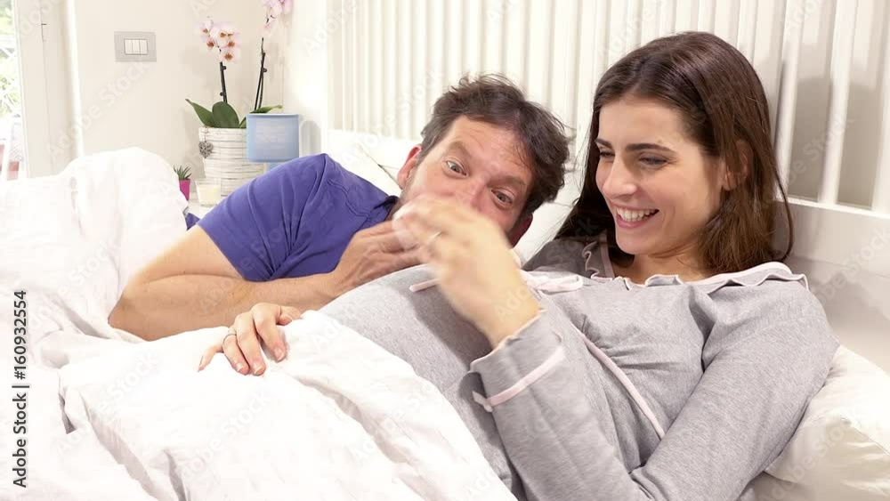 Happy pregnant woman in bed talking smiling and laughing with husband closeup Happy pregnant woman in bed talking smiling and laughing with husband closeup