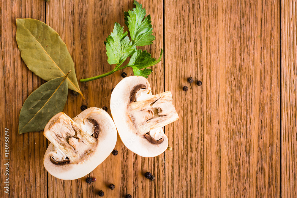Halved fresh button champignons, bay leaf and parsley on a wooden table. Top view Halved fresh button champignons, bay leaf and parsley on a wooden table. Top view