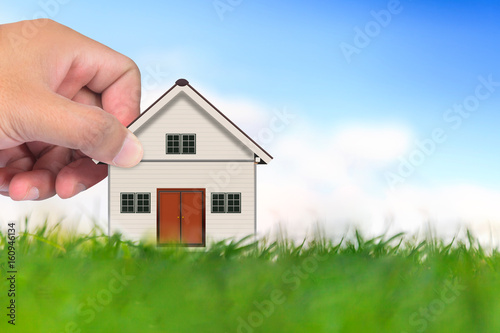 Hand and Small house on green grass under the blue sky