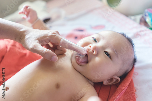 Asain doctor ,nurse or Mother use finger to clean baby tongue and gum with the clean gauze, first brushing teeth during bathing time.vintage color © Have a nice day 