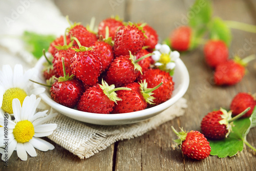 Sweet wild strawberries in plate with daisies on wooden background