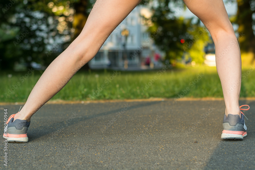 Runner stretches leg on tarmac with running shoes from behind Runner stretches leg on tarmac with running shoes from behind
