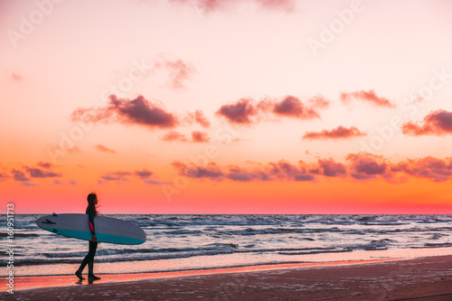 Girl with surfboard on beach at sunset or sunrise. Surfer and ocean