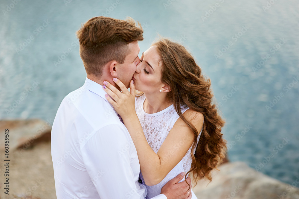Bride and groom sitting on the beach and kissing