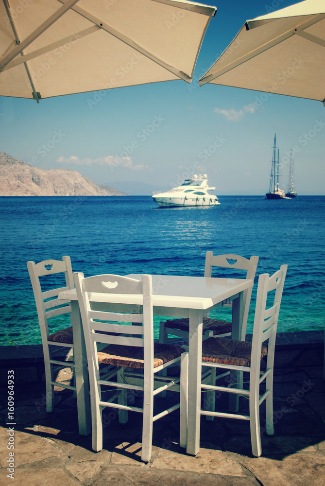 Wooden table and chairs by the sea, on the pier, in the distance you can see large and expensive yachts at sea