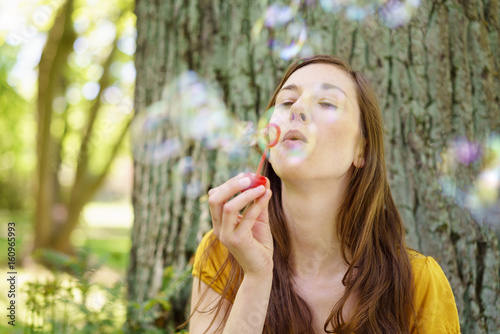 Happy young woman blowing bubbles in a park