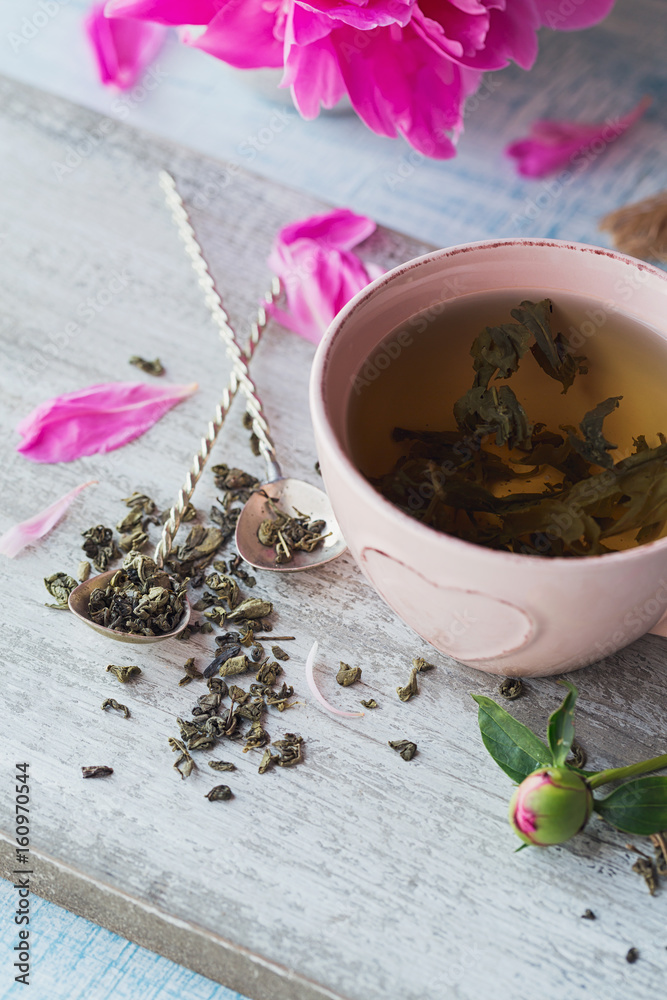Still life with pink peony flowers and a cup of herbal or green tea Still life with pink peony flowers and a cup of herbal or green tea