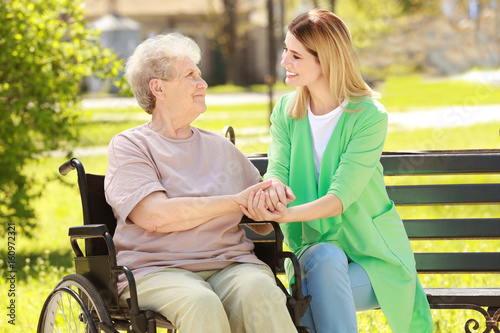 Bild auf Leinwand Disabled elderly woman and young caregiver in park on sunny day