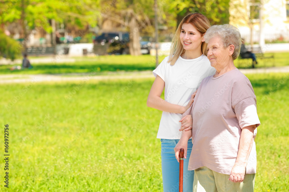 Elderly woman and young caregiver in park on sunny day Elderly woman and young caregiver in park on sunny day