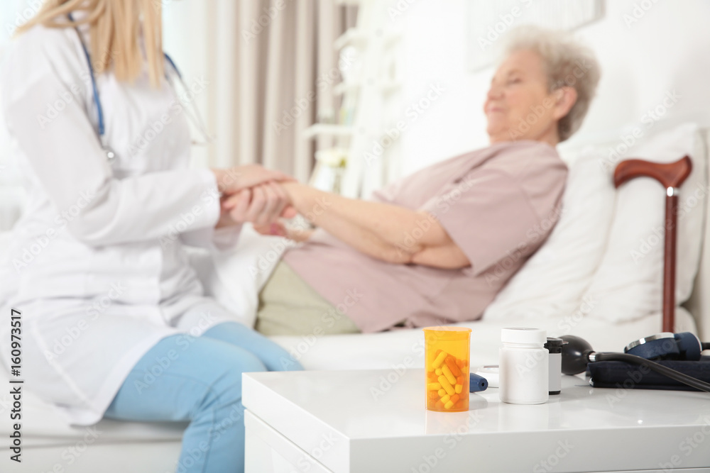 Fototapeta premium Night stand with medicines and blurred nurse examining elderly woman on background