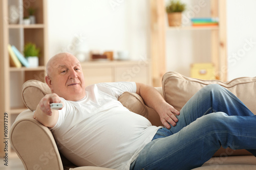 Canvastavla Fat senior man watching TV while lying on sofa at home