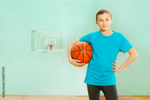 Happy girl standing with basket ball in gym