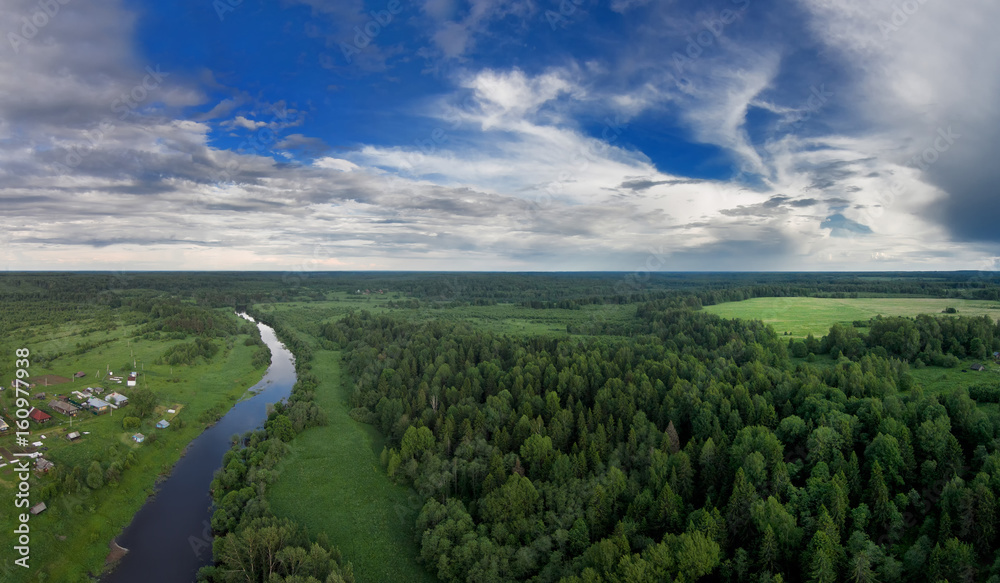 A small village on one side of the river, and on the other side of the forest. Beautiful blue sky with white clouds. Evening. The Sot River. A bird's-eye view. Yaroslavl region. Russia