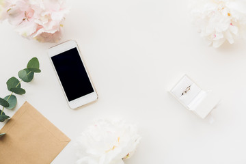 Wedding ring in white gift box on background of flowers and phone. top view