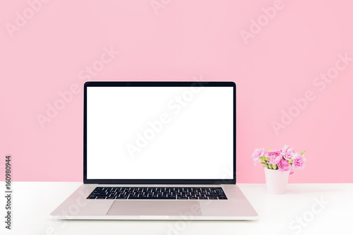 Laptop with white blank screen and flowers in vase on table on pink background. mock up