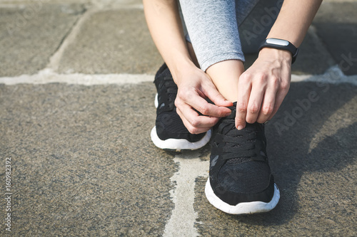 Girl runner tying laces for jogging her shoes on road in a park. Running shoes, Shoelaces, Urban jogger, Exercise concept. Sport lifestyle. close up of woman tying shoelaces outdoors