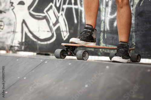 Young female skater standing on skateboards at the skate park on ramp.Only legs and board are visible.