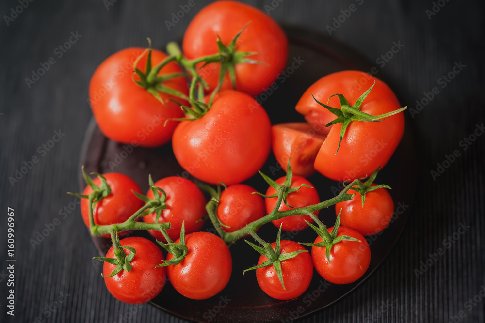 Fresh red ripe tomatoes with water drops on branches on black background. Close-up. Selective focus. Top view. Low key. Concept of vegetarian, healthy food.