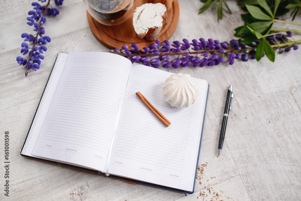 Fototapeta premium Note with a pen, a calendar and a Cup of coffee served with bruschetta, lupins flowers on wooden table