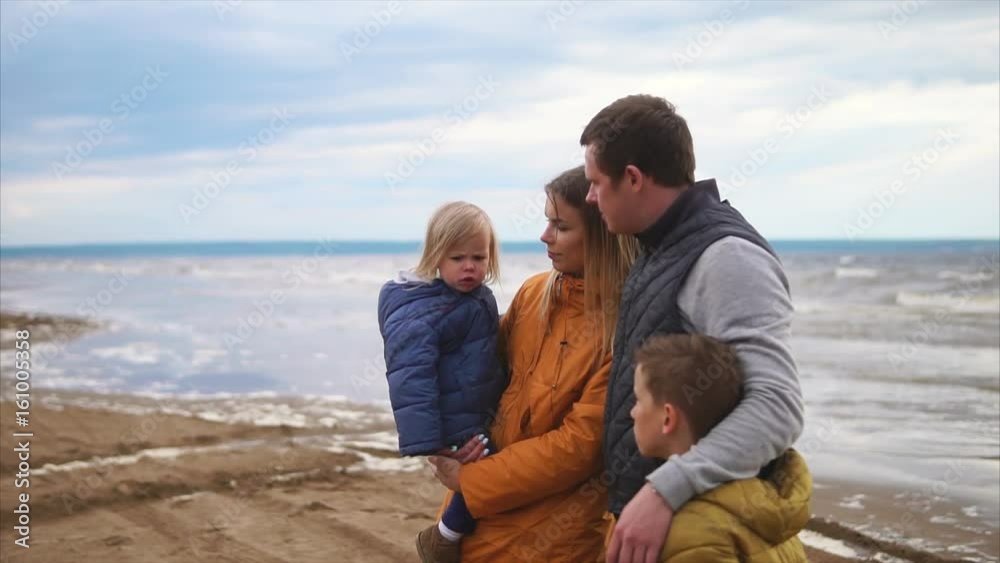 Family leisure. Family of four standing on a beach at cold windy weather. Woman, man, girl and boy Family leisure. Family of four standing on a beach at cold windy weather. Woman, man, girl and boy