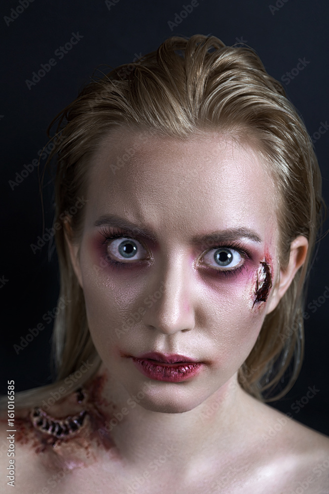A young blonde girl with blue eyes with a scar on her cheek and a bite on her shoulder. Dark blue background. She is scarried A young blonde girl with blue eyes with a scar on her cheek and a bite on her shoulder. Dark blue background. She is scarried