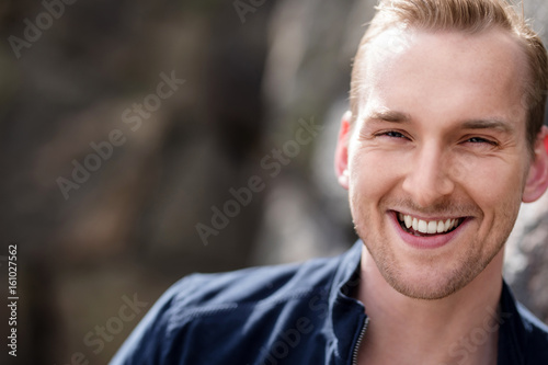 Happy laughing man wearing blue leather jacket standing outside on a sunny day.