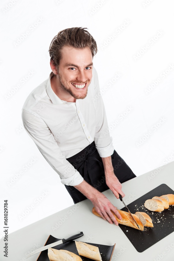 Smiling attractive home chef slicing bread wearing a white shirt and black apron standing against a white background. Smiling attractive home chef slicing bread wearing a white shirt and black apron standing against a white background.