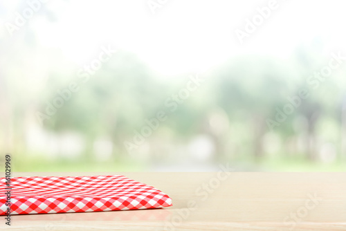 Red checkered cloth on wood table top in blur green background of trees in the park