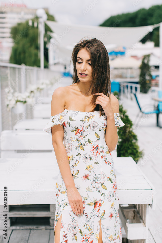 Portrait of a beautiful woman in a dress posing on a white wooden beach of summer.