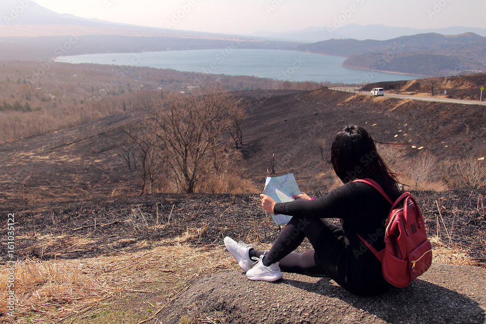 Traveler woman sitting at the mountain surrounded by beautiful natural to studying the route from maps in hand to find attractions in Japan. Travel and active lifestyle concept