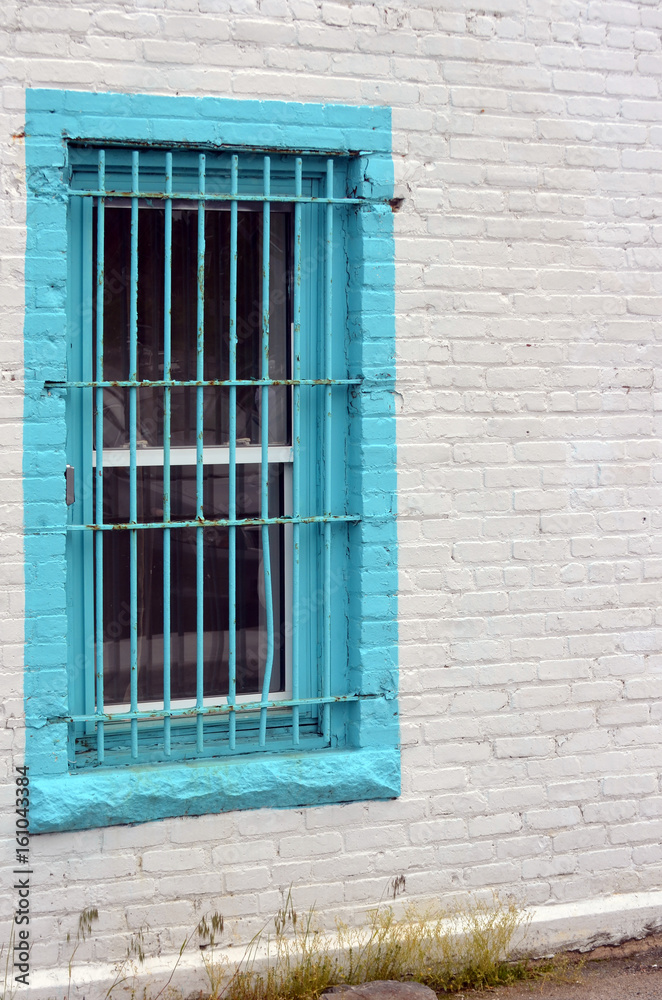 Turquoise window with bars on white brick building 