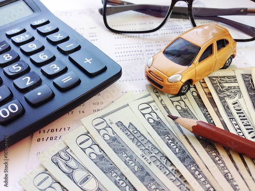 Business, finance, savings, banking or car loan concept : Miniature car model, pencil, money, calculator, eyeglasses and savings account passbook or financial statement on white background