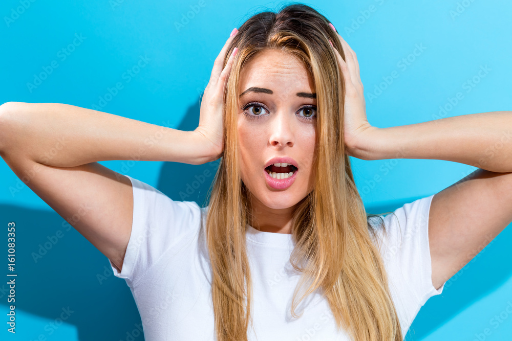 Young woman blocking her ears on a blue background