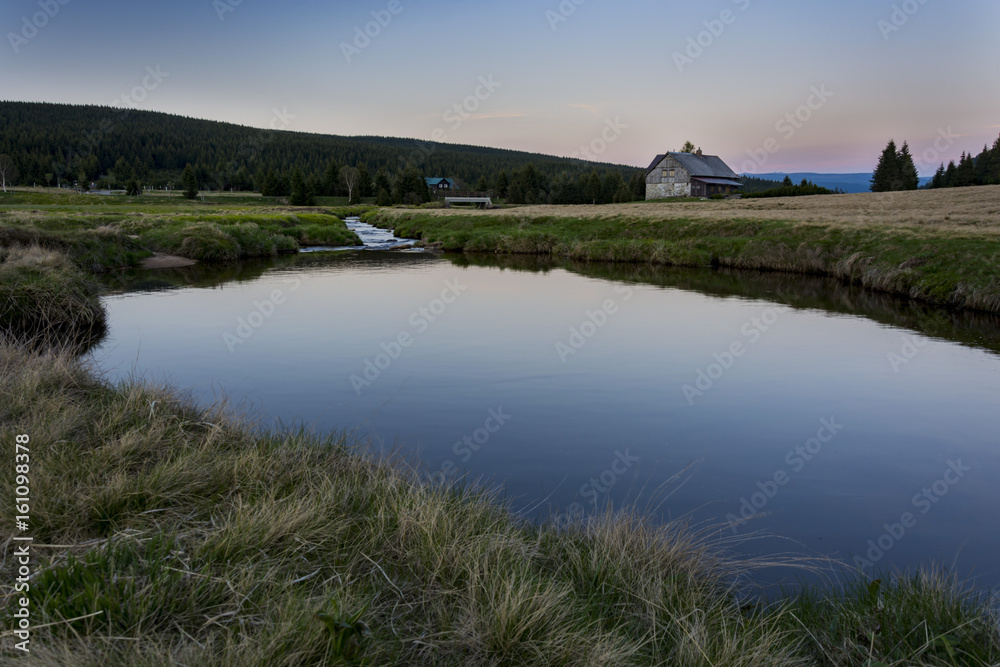 Small lake with clear water. Reflection of blue sky. Small house behind the lake during sunset. Czech nature.