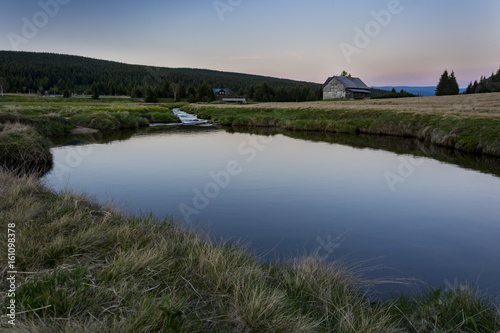 Small lake with clear water. Reflection of blue sky. Small house behind the lake during sunset. Czech nature.