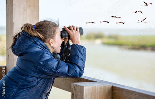 Girl with a winter jacket watching through binoculars from a wooden balcony photo